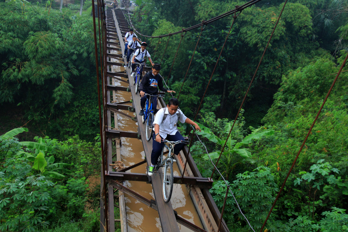 Sejumlah siswa melintasi jembatan gantung untuk saluran irigasi yang membentang di atas sungai perbatasan Kabupaten Boyolali-Kabupaten Karanganyar di dusun Plempungan, Desa Bolon, Kacamatan Colomadu, Karanganyar, Jawa Tengah, Selasa (23/2). Meski berbahaya, jembatan saluran irigasi yang dibangun sejak zaman kolonial Belanda itu menjadi akses pilihan warga dan anak-anak sekolah untuk menyeberang antar dua wilayah karena menyingkat jarak perjalanan hingga 8 kilometer. ANTARA FOTO/Maulana Surya/ama/16.