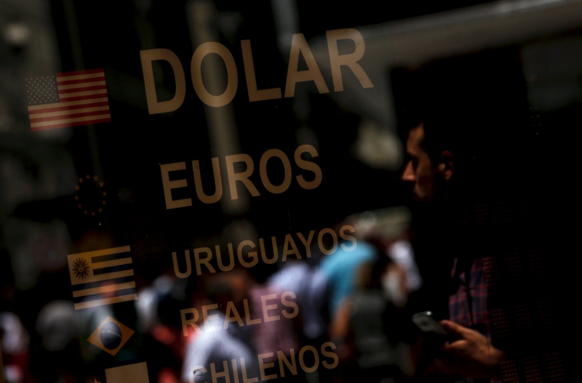People are reflected on a window with a currency exchange rates board at a money exchange in Buenos Aires' financial district, Argentina, December 16, 2015. Argentina will announce a much anticipated relaxation of currency controls on Wednesday, the government said, setting the stage for a weakening of the local peso and an increase of soybean shipments from the world's No. 3 exporter. REUTERS/Marcos Brindicci TPX IMAGES OF THE DAY
