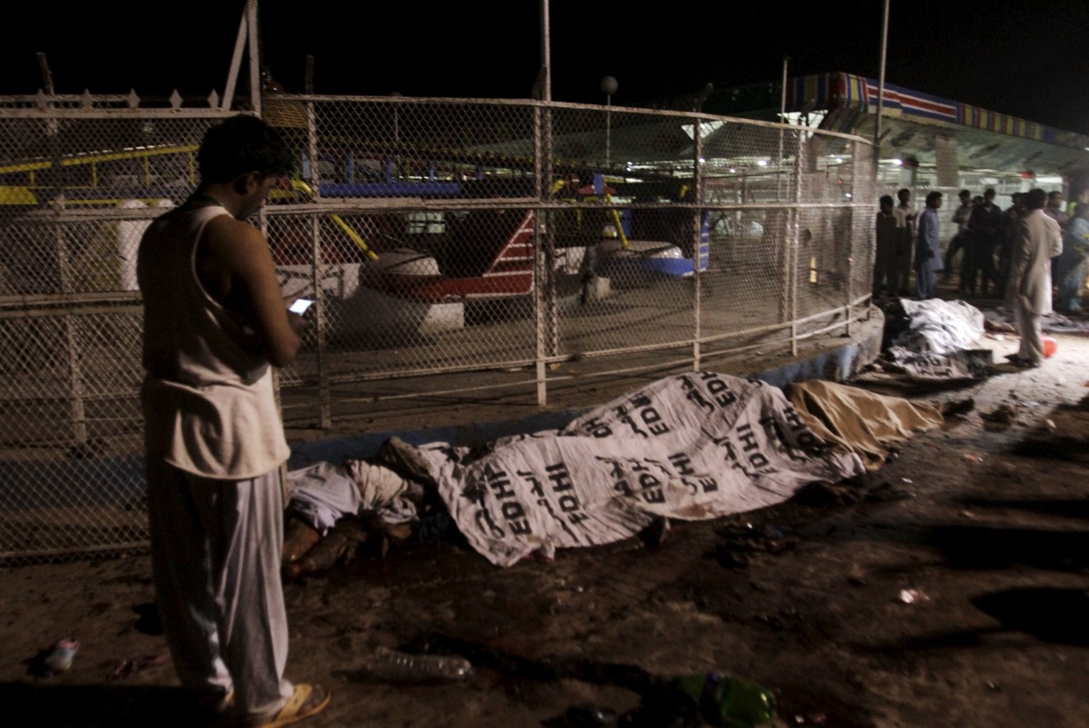 ATTENTION EDITORS - VISUAL COVERAGE OF SCENES OF INJURY OR DEATH.A man (R) uses his mobile phone as he stands next to bodies covered in sheets at the site of a blast, outside a public park in Lahore, Pakistan, March 27, 2016. REUTERS/Mohsin Raza