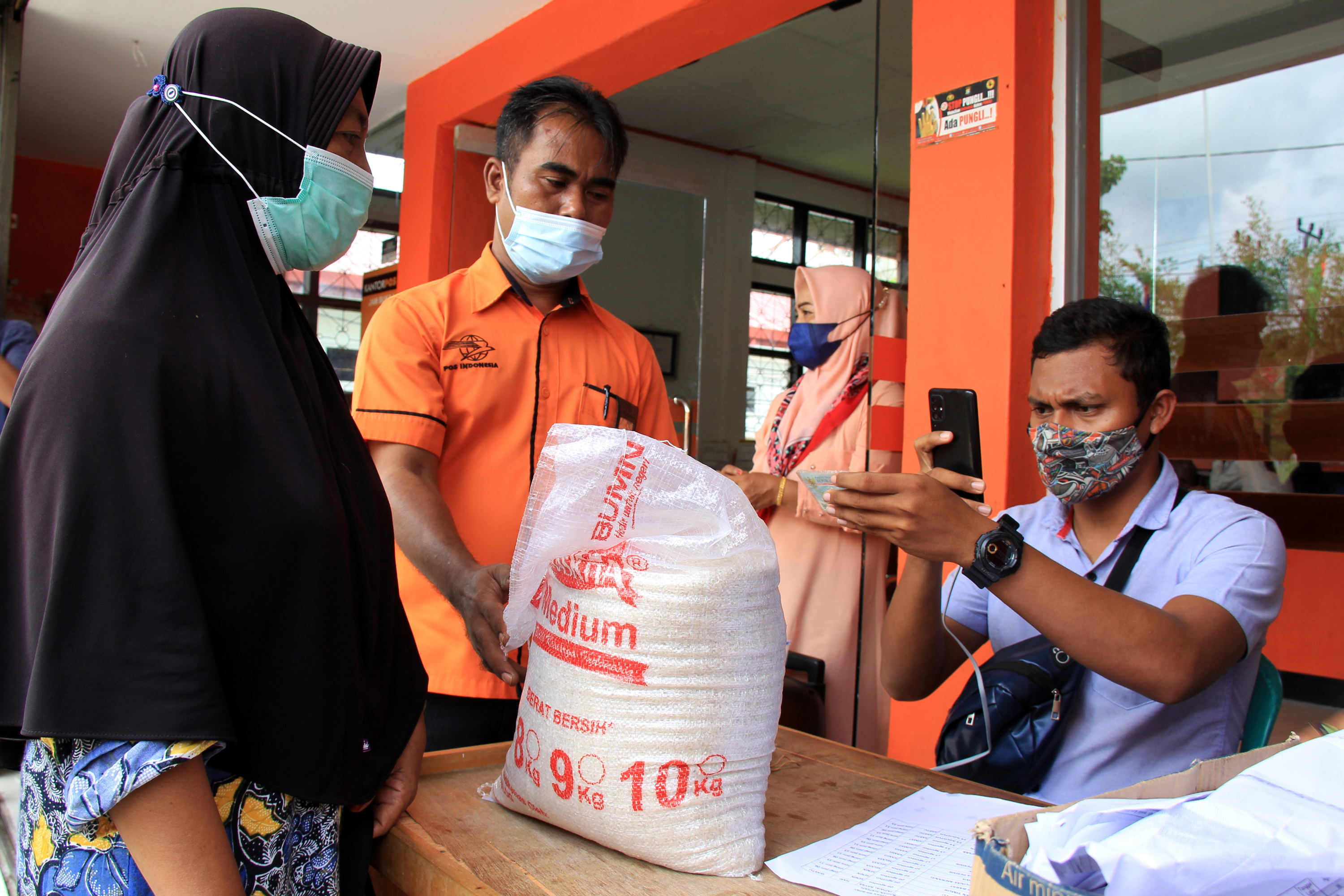 Petugas memotret kartu identitas warga penerima bantuan sosial (bansos) beras dari pemerintah di Kantor Pos Bagansiapiapi, Rokan Hilir, Riau, Selasa (10/8/2021). ANTARA FOTO/Aswaddy Hamid/rwa. DISTRIBUSI BANSOS BERAS DI ROKAN HILIR