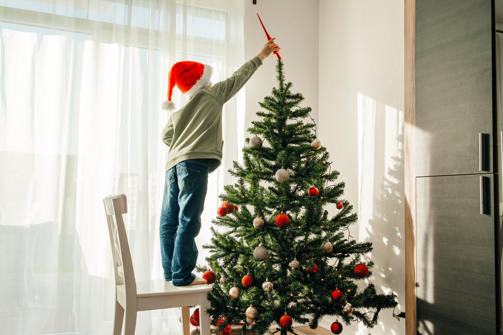 Anak laki-laki bertopi sinterklas menghiasi pohon Natal. FOTO/iStockphoto Anak menghiasi pohon Natal