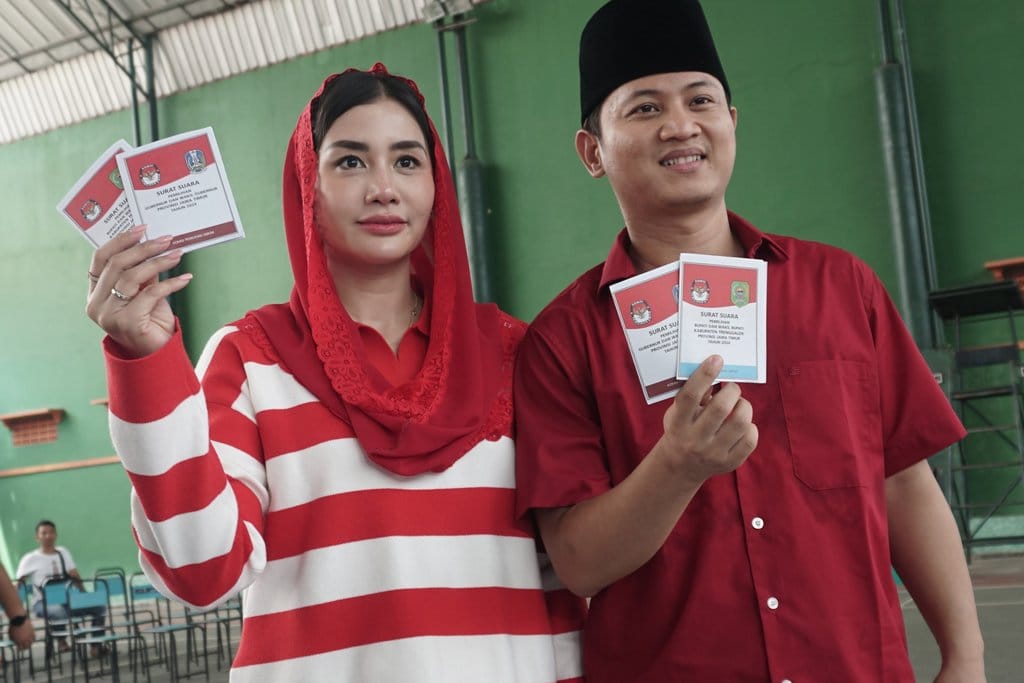 Petahana Bupati Trenggalek Mochamad Nur Arifin (kanan), didampingi istrinya Novita Hardini (kiri) menunjukkan surat suara yang akan dicoblos di TPS 02 Kelurahan Surondakan, Trenggalek, Jawa Timur, Rabu (27/11/2024). Mochamad Nur Arifin yang berpasangan dengan wakilnya Syah Muhammad Natanegara maju pada Pilkada Trenggalek 2024 sebagai calon tunggal melawan kotak kosong. ANTARA FOTO/Destyan Sujarwoko/aww. Pilkada calon tunggal di Trenggalek