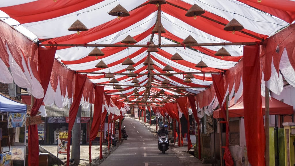 Pengendara sepeda motor melintas di jalan yang bagian atasnya dihiasi kain merah putih di Kampung Cibahong, Desa Sukamenak, Kecamatan Sukarame, Kabupaten Tasikmalaya, Jawa Barat, Rabu (6/8/2025). ANTARA FOTO/Adeng Bustomi/tom. Pemasangan kain merah putih sepanjang 250 meter di Tasikmalaya