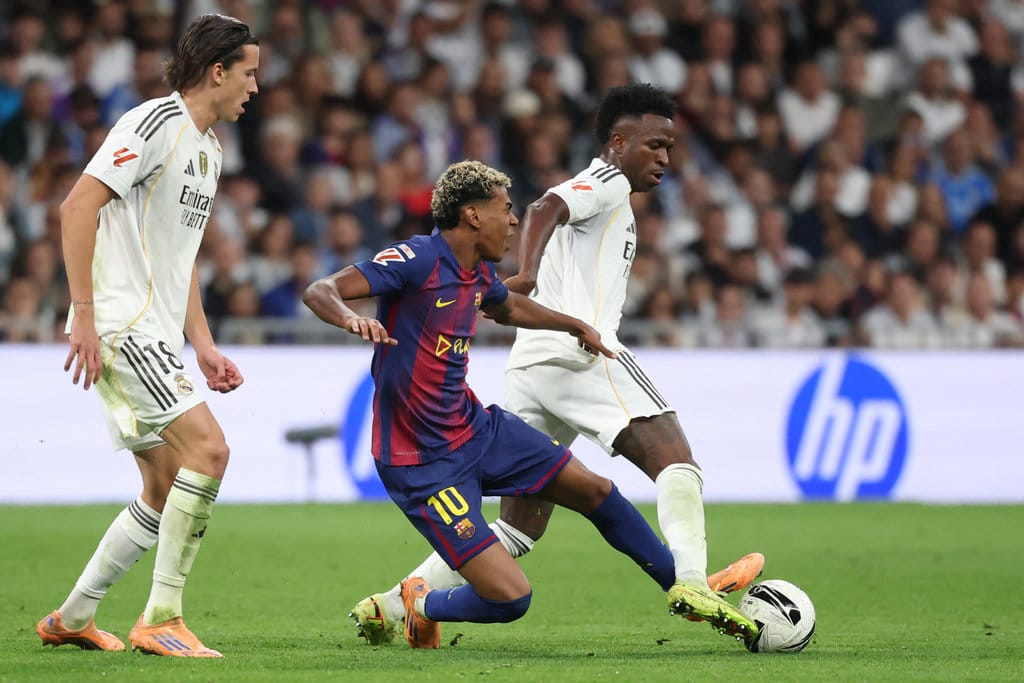 Penyerang Barcelona asal Spanyol 10 Lamine Yamal (tengah) dan penyerang Real Madrid asal Brasil 07 Vinicius Junior (kanan) berebut bola dalam pertandingan Liga Spanyol antara Real Madrid CF dan FC Barcelona di Stadion Santiago Bernabeu, Madrid, pada 26 Oktober 2025. (Foto oleh Oscar DEL POZO / AFP) Lamine Yamal vs Vinicius