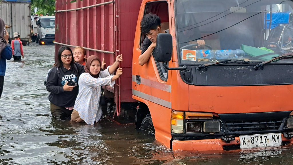 Beberapa perempuan ikut mendorong truk yang mogok saat melewati banjir di Jalan Kaligawe Semarang, Rabu (29/10/2025). Tirto.id/Baihaqi Annizar Banjir Semarang