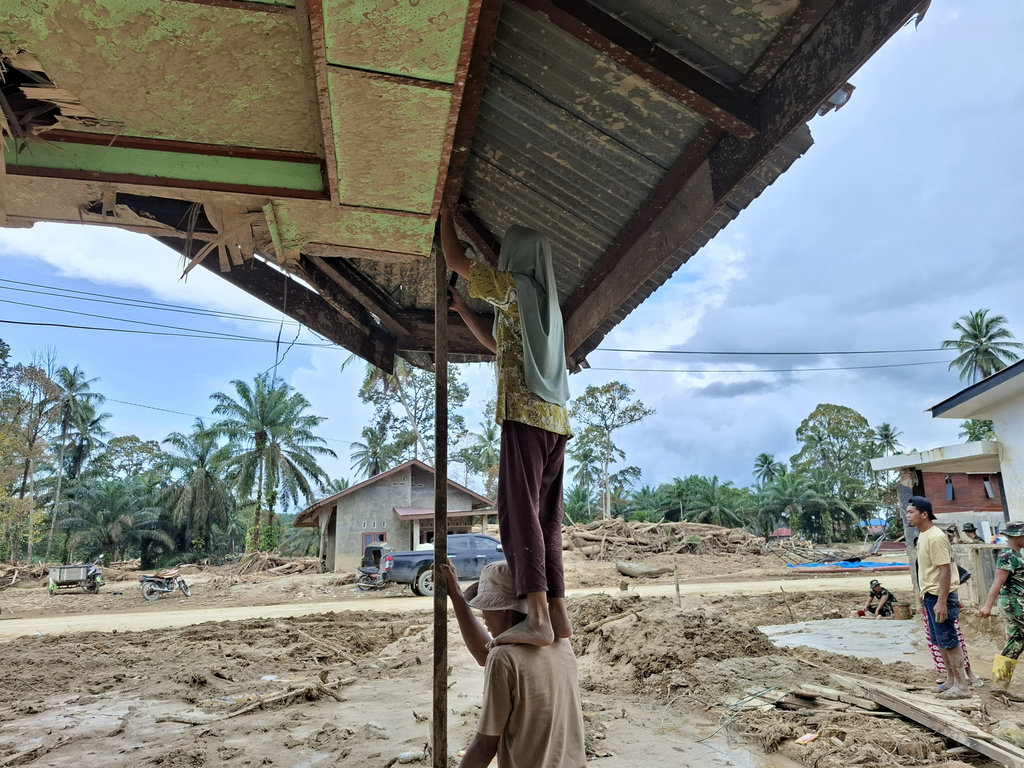 Pasangan suami istri Abdul Salam dan Nurbaeti sedang memperbaiki rumah mereka yang tersisa sepaeuh bangunan di Desa Garoga, Kecamatan Batang Toru, Tapanuli Selatan pada Sabtu (6/12/2025). tirto.id/M. Irfan Al Amin Kisah Suami Istri memperbaiki Rumah di Tapanuli Selatan