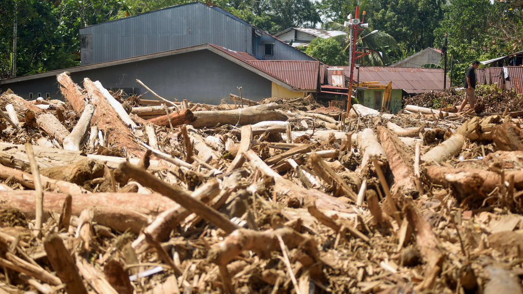 Warga melintas di antara tumpukan gelondongan kayu di permukiman di Tabiang Bandang Gadang, Nanggalo, Padang, Sumatera Barat, Selasa (9/12/2025). ANTARA FOTO/Iggoy el Fitra/tom. Tumpukan kayu gelondongan di permukiman