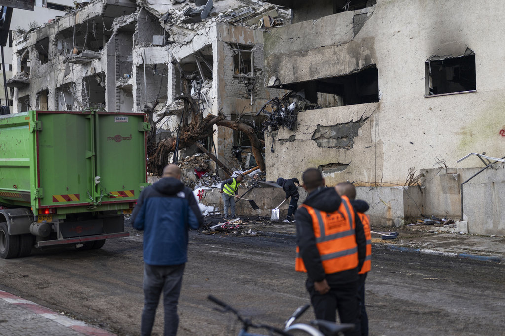 Para pekerja membersihkan puing-puing di depan sebuah bangunan yang rusak akibat serangan Iran yang dilaporkan terjadi semalam di Tel Aviv pada 1 Maret 2026. (Photo by Ilia YEFIMOVICH / AFP) Serangan Iran ke Tel Aviv