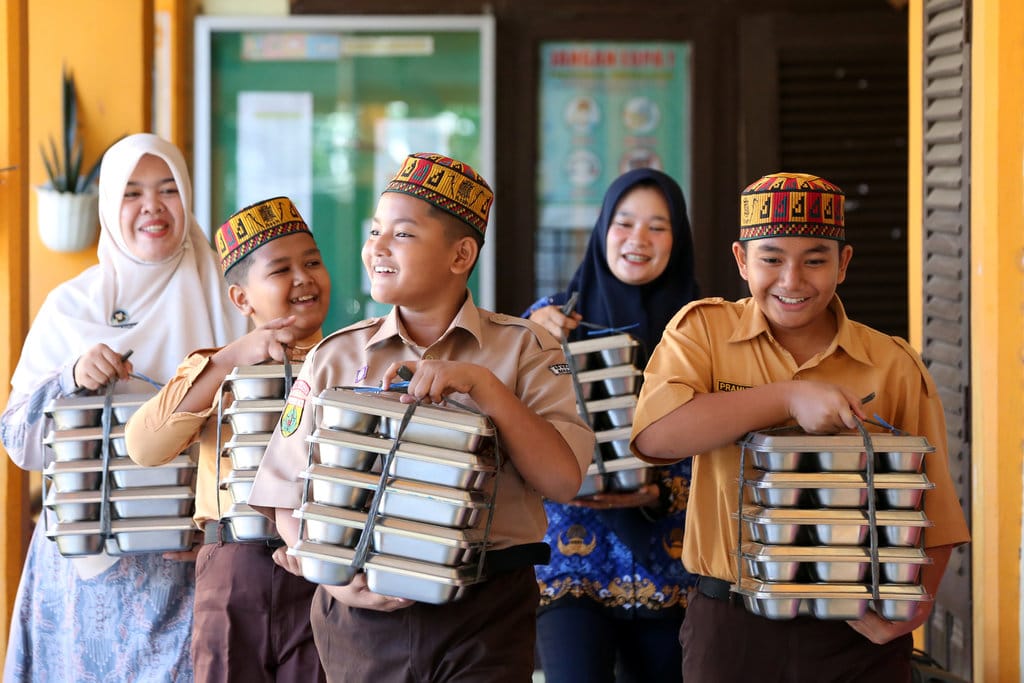 Pelajar bersama petugas Satuan Pelayanan Pemenuhan Gizi (SPPG) Ie Masen Ulee Kareng dan guru membawa paket Makan Bergizi Gratis (MBG) untuk dibagikan kepada peserta Masa Pengenalan Lingkungan Sekolah (MPLS) di SD Negeri 11 Banda Aceh, Aceh, Jumat (17/7/2026). Sebanyak 25 SPPG kembali beroperasi untuk menyalurkan MBG kepada 7.350 pelajar yang mengikuti MPLS jenjang SD dan SMP, 75.650 pelajar lainnya, serta ibu hamil, ibu menyusui, dan balita di Kota Banda Aceh sebagai upaya mendukung terwujudnya Indonesia Emas 2045. ANTARA FOTO/Irwansyah Putra/kye SPPG kembali salurkan Makan Bergizi Gratis di Banda Aceh