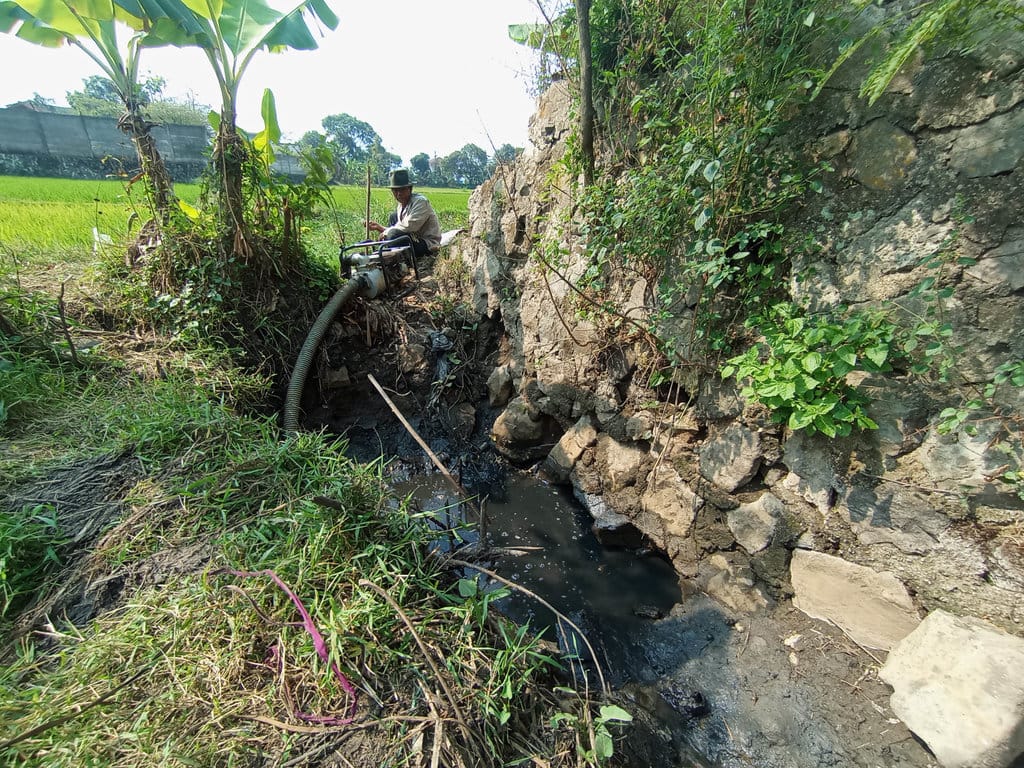 Petani, Saepudin (62) saat berkegiatan di sawah lahan garapan, Kecamatan Gedebage, Kota Bandung, Kamis (23/7/2026). Dia berulangkali memastikan ketersediaan air dari parit selokan dan sumur buatan sederhana. Muhamad Nizar/tirto.id. Saepudin