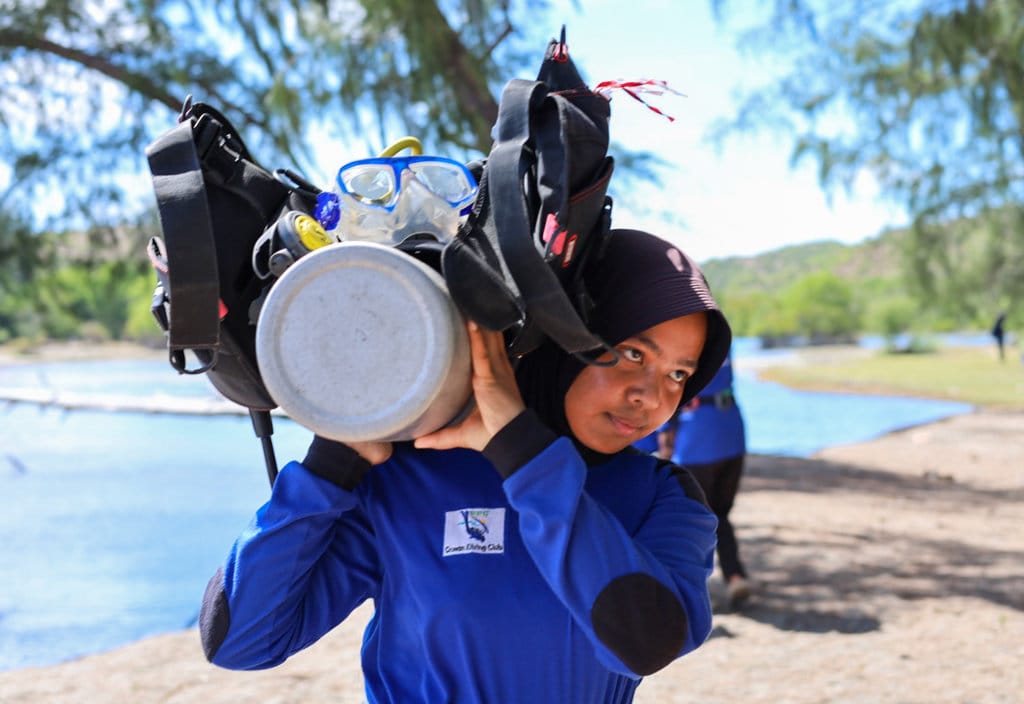 Dedek Riani memikul tabung selam di pantai Krueng Raya, Aceh Besar, Sabtu (15/8/2026). Foto : Firhan Farabi/tirto.id Bendera Merah Putih Berkibar di Laut Krueng Raya
