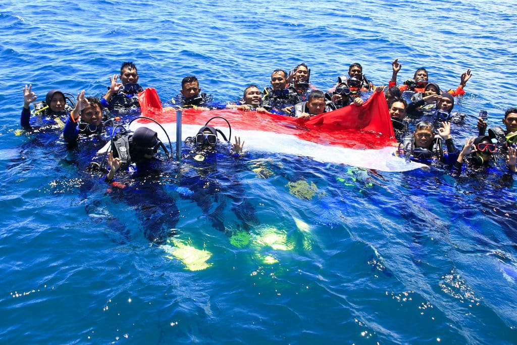 Para penyelam membentangkan bendera merah putih dipermukaan laut di Krueng Raya, Aceh Besar, Sabtu (15/8/2026). Foto : Firhan Farabi/tirto.id Bendera Merah Putih Berkibar di Laut Krueng Raya