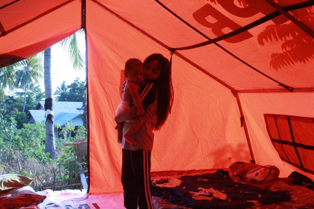 Seorang anak SDK Cawalo dan balita yang digendong di posko pengungsian Desa Rokirole, Kecamatan Palue, Kabupaten Sikka, Rabu (16/9/2026) sore. (Foto: Mario Sina) Newsplus 32 Hari Pascagempa Flores