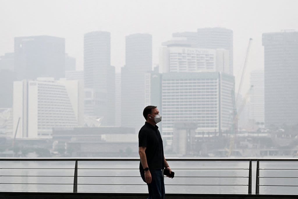 (DOKUMENTASI) Seorang pejalan kaki yang mengenakan masker berjalan di sepanjang kawasan Marina Bay, sementara gedung-gedung tampak diselimuti kabut asap di Singapura pada 12 Oktober 2026. (Foto oleh Roslan RAHMAN / AFP) kabut asap di Singapura