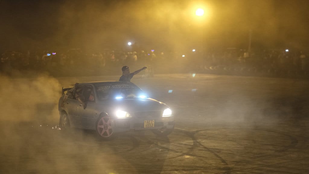 Seorang pria memberi isyarat saat ia mencondongkan tubuh ke luar mobil yang sedang berputar-putar dalam sebuah acara *spinners* di sebuah arena untuk pertemuan lintas komunitas pada Malam Tahun Baru di Bulawayo, 31 Desember 2025. (Photo by Zinyange Auntony / AFP) Spinning Afrika Selatan