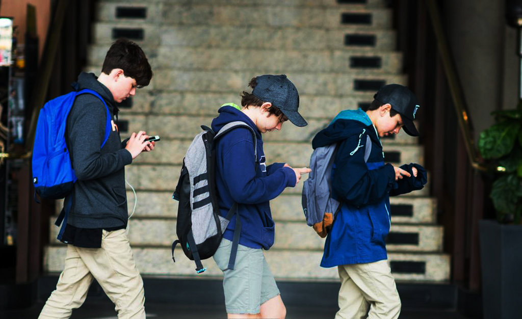 Tiga orang anak sedang berjalan sambil mengamati layar smartphonenya. Foto/Getty Images APLIKASI SMARTPHONE