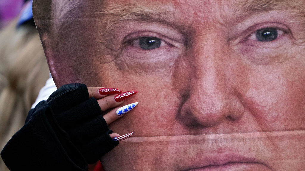 Seorang pendukung Trump dengan tampilan kuku uniknya, memegang potongan wajah gambar Presiden Donald Trump saat aksi massa 'Save America Rally' pada Rabu, 6 Januari 2021, di Washington. AP / Jacquelyn Martin Massa Pendukung Trump Serbu Capitol