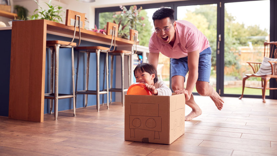 Ilustrasi Ayah mendorong anak di sekitar lantai dapur di rumah dengan mobil kardus. FOTO/iStockphoto Ilustrasi peran ayah pada anak