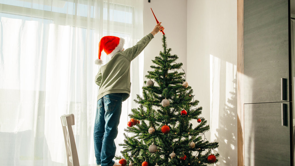 Anak laki-laki bertopi sinterklas menghiasi pohon Natal. FOTO/iStockphoto Anak menghiasi pohon Natal