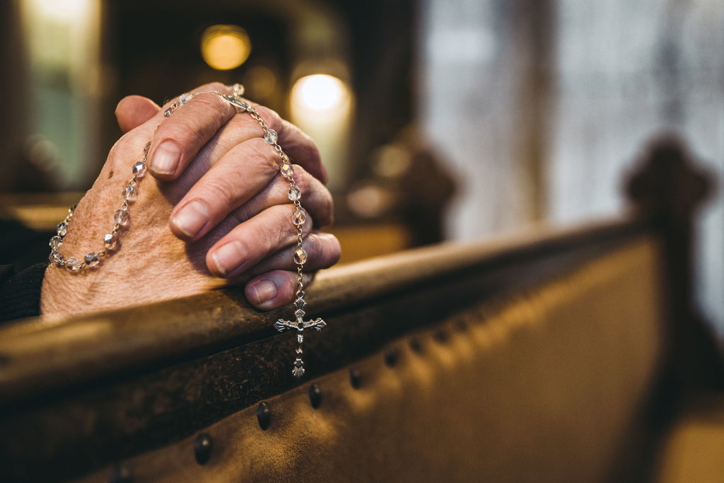 Praying senior hands with rosary in church bench Doa Kerahiman Ilahi