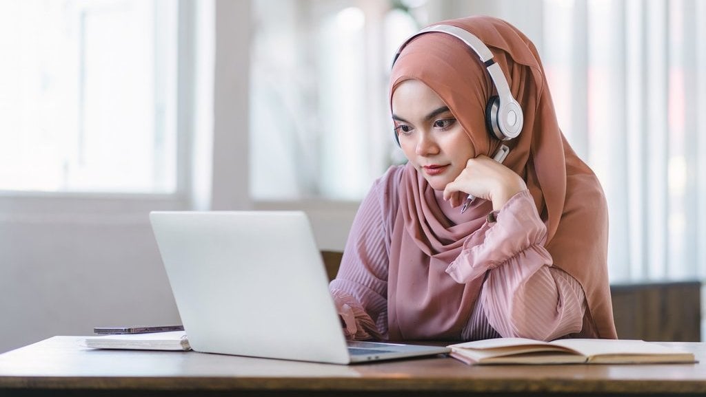 Perempuan berjilbab menghadap laptop