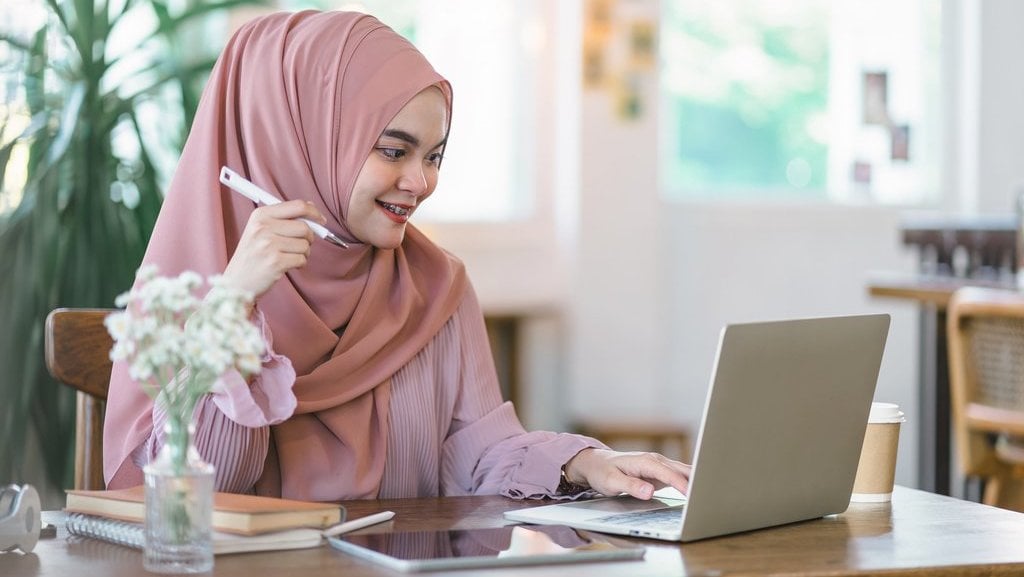 Perempuan berjilbab menghadap laptop