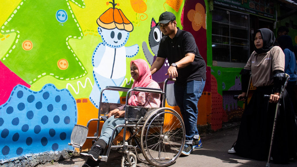 Relawan mendorong warga penyandang disabilitas daksa dengan menggunakan kusi roda untuk melukis mural di Kampung Binong Jati, Bandung, Jawa Barat, Sabtu (14/6/2025). ANTARA FOTO/Novrian Arbi/YU Mural bersama perempuan disabilitas