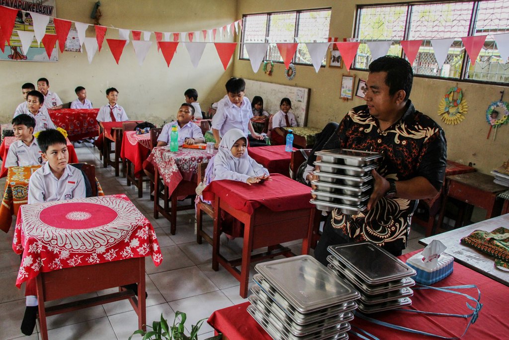Seorang guru bersiap membagikan makanan bergizi gratis kepada siswa di SD Negeri 10 Palangka Raya, Kalimantan Tengah, Selasa (8/7/2025). ANTARA FOTO/Auliya Rahman/tom. Realisasi anggaran program MBG semester-I 2025