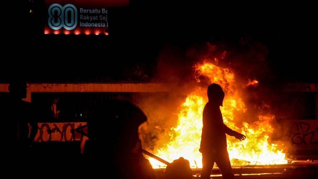 Pengunjuk rasa berjalan di sebelah pembatas jalan yang dibakar saat aksi di Jakarta, Jumat (29/8/2025). ANTARA FOTO/Putra M. Akbar/rwa. Aksi unjuk rasa di depan DPR