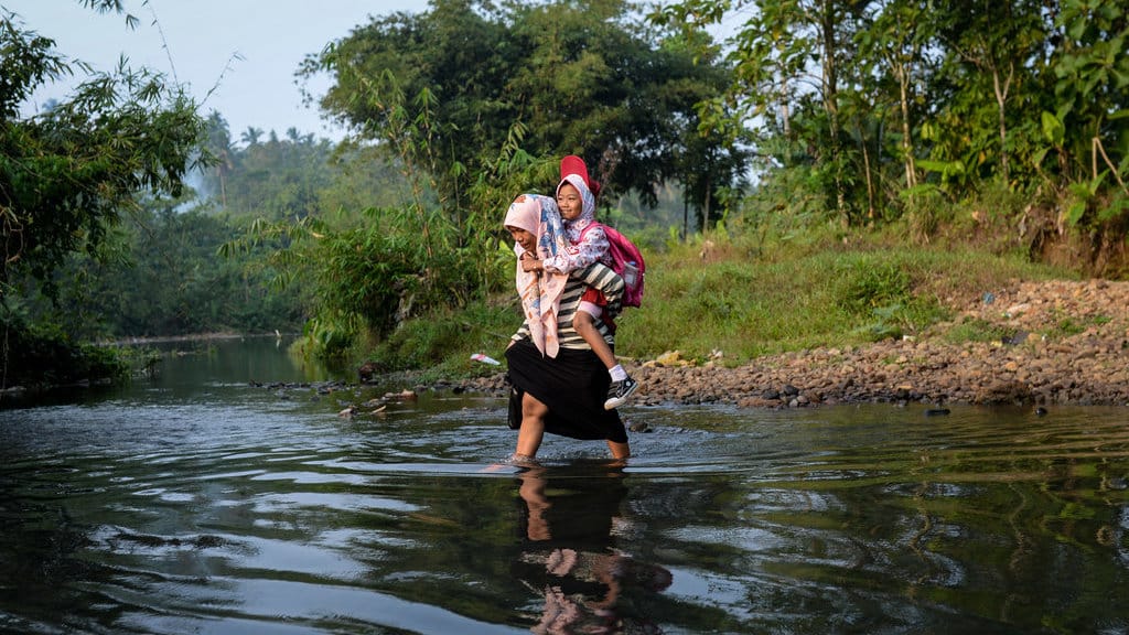 siswa SD Negeri Padahayu 2 menggendong anaknya menyeberangi Sungai Cipunten Agung di Cikedal