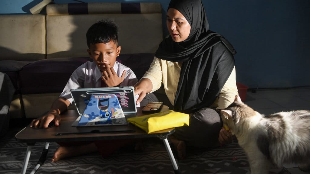 Siswa Sekolah Dasar Negeri 07 Rorotan Pagi, Richie Archilles (kiri), didampingi orang tuanya mengikuti pembelajaran secara daring dari rumah di Jakarta Utara, Senin (7/9/2026). Pemprov DKI Jakarta memberlakukan pembelajaran jarak jauh (PJJ) bagi siswa PAUD, SKB/PKBM, SLB, SD, SMP, SMA, dan SMK negeri maupun swasta sebagai langkah antisipasi untuk melindungi anak-anak dari paparan abu vulkanik akibat erupsi Gunung Anak Krakatau. ANTARA FOTO/M Risyal Hidayat/tom. Penerapan PJJ imbas abu vulkanik erupsi Anak Krakatau