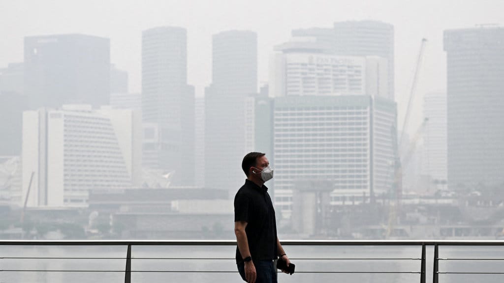 (DOKUMENTASI) Seorang pejalan kaki yang mengenakan masker berjalan di sepanjang kawasan Marina Bay, sementara gedung-gedung tampak diselimuti kabut asap di Singapura pada 12 Oktober 2026. (Foto oleh Roslan RAHMAN / AFP) kabut asap di Singapura